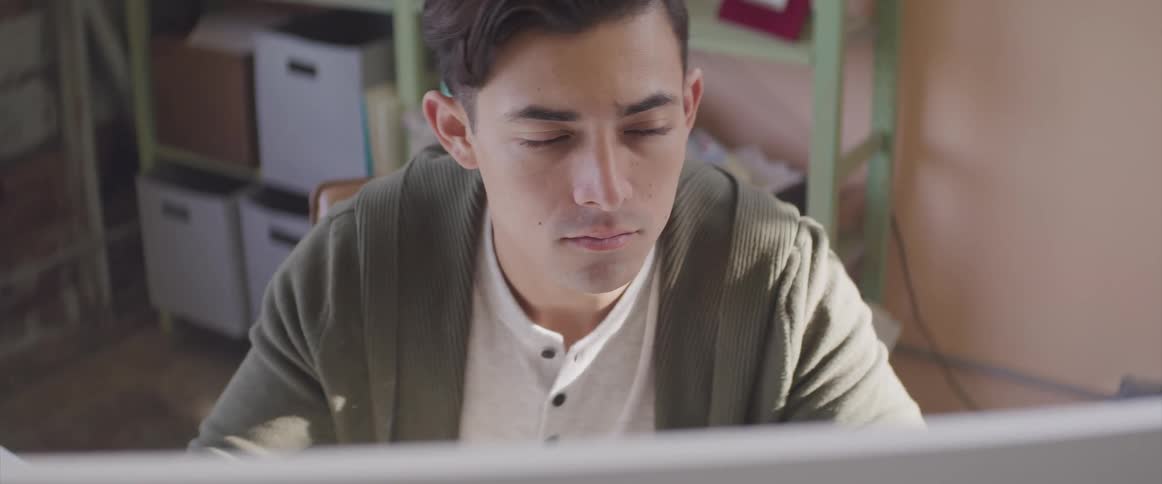 Young man thinks while working from home on a computer