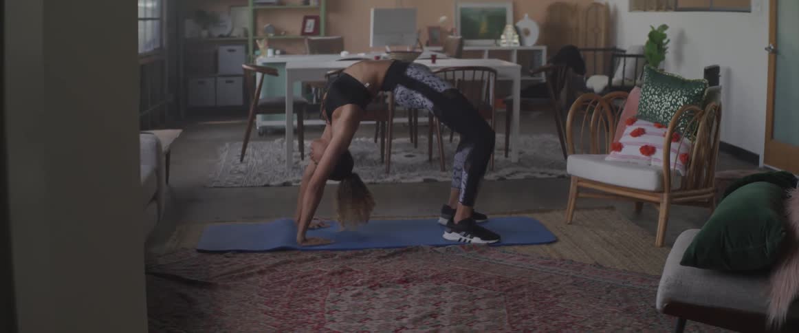 A woman holds a backbend pose while doing yoga in her decorated living room