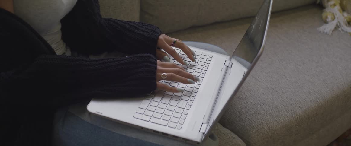 Woman with a long sleeve black coat sitting on a sofa uses a laptop in the living room