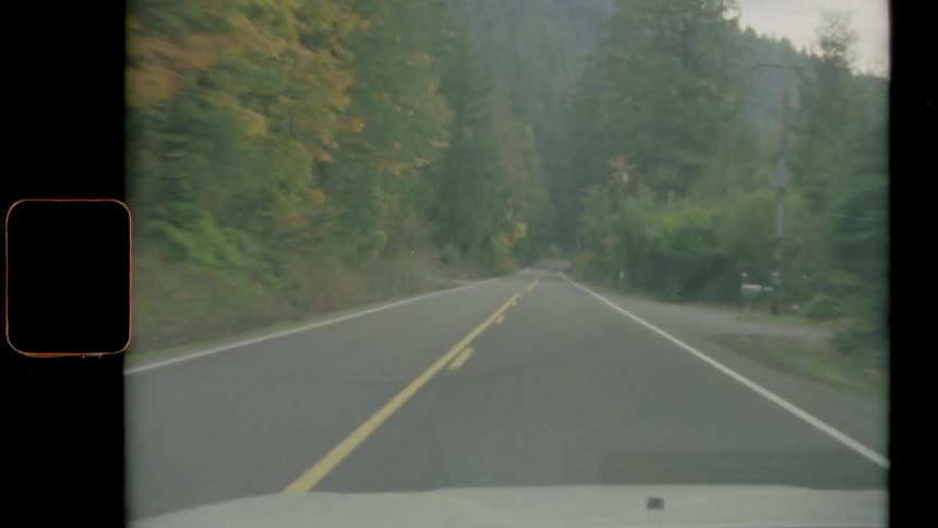 A vehicle is driving down a fall foliage tree lined mountainside