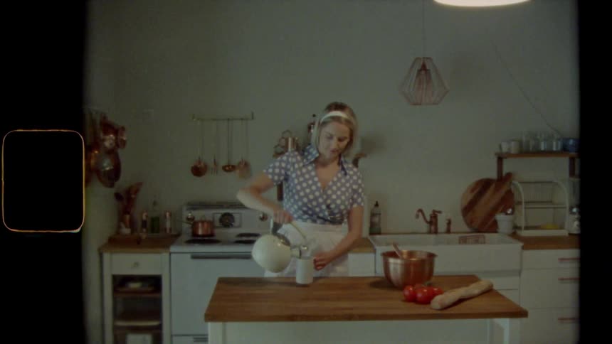 A woman pours a liquid from a teapot into a glass while standing in the kitchen