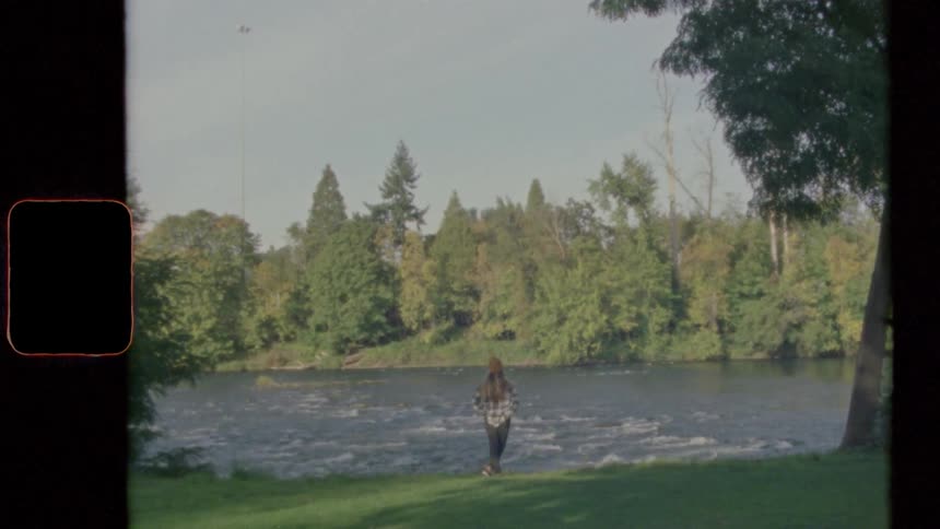 Woman with long hair and jeans stands on the bank of river