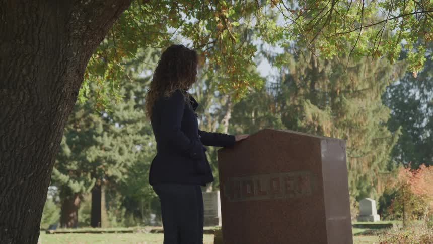 A woman dressed in black stands with her hand on a headstone