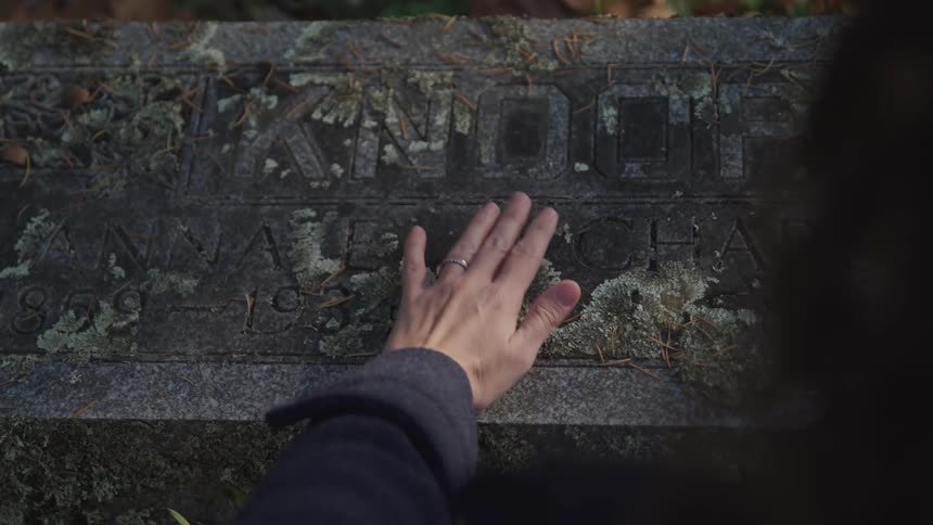 A person with a ring on their hand rubbing a tombstone