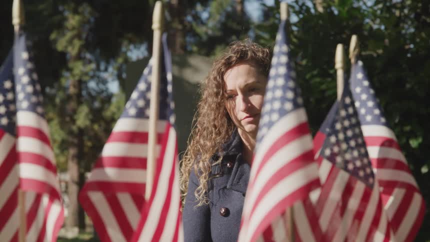 Woman visits a tomb covered in american flags in a cemetery