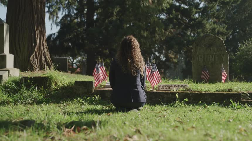 Woman crouches near grave decorated with small american flags