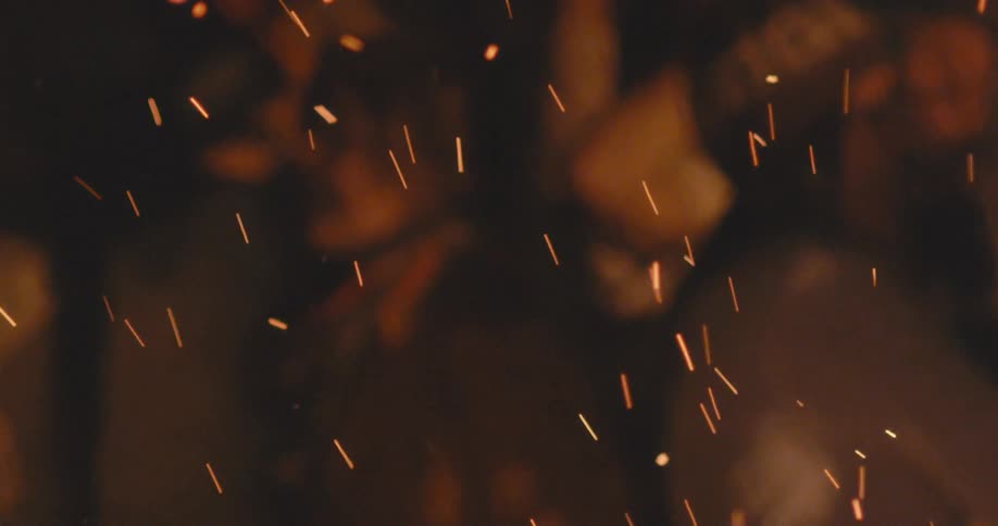 People dancing in front of the soaring sparks of a a bonfire outdoors at night