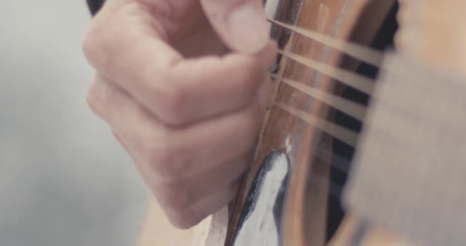 A guitarist strumming on an acoustic guitar in macro as it snows