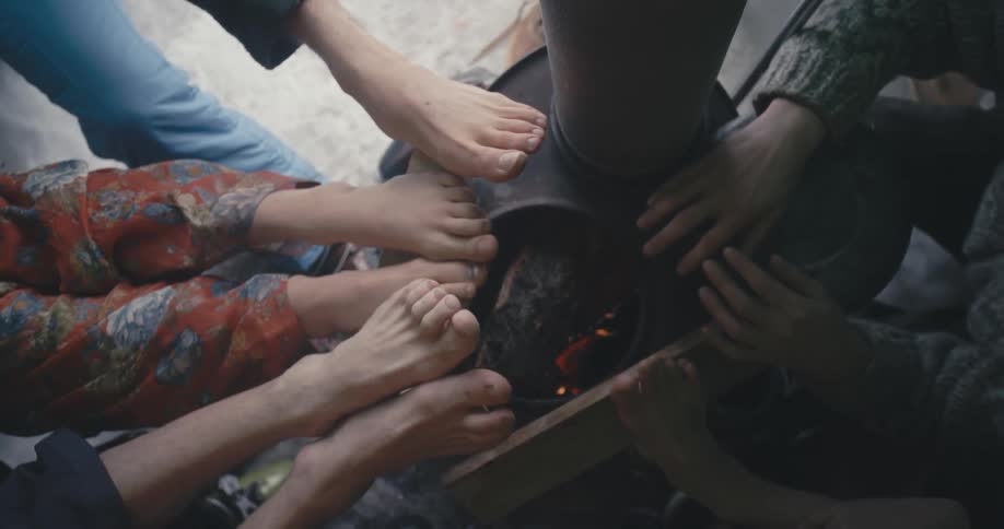 People warm their bare feet and hands near wood burning stove with chimney