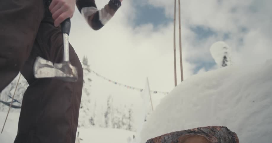 A woman chops wood with her hatchet on a cloudy winter day