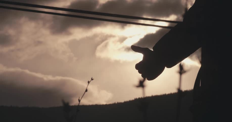 The silhouette of a hitchhiker standing by the side of the road as cars whiz by