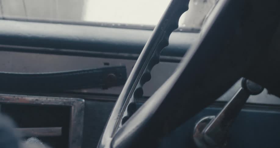 Man in a sweater drives an old truck with his hands on the wheel