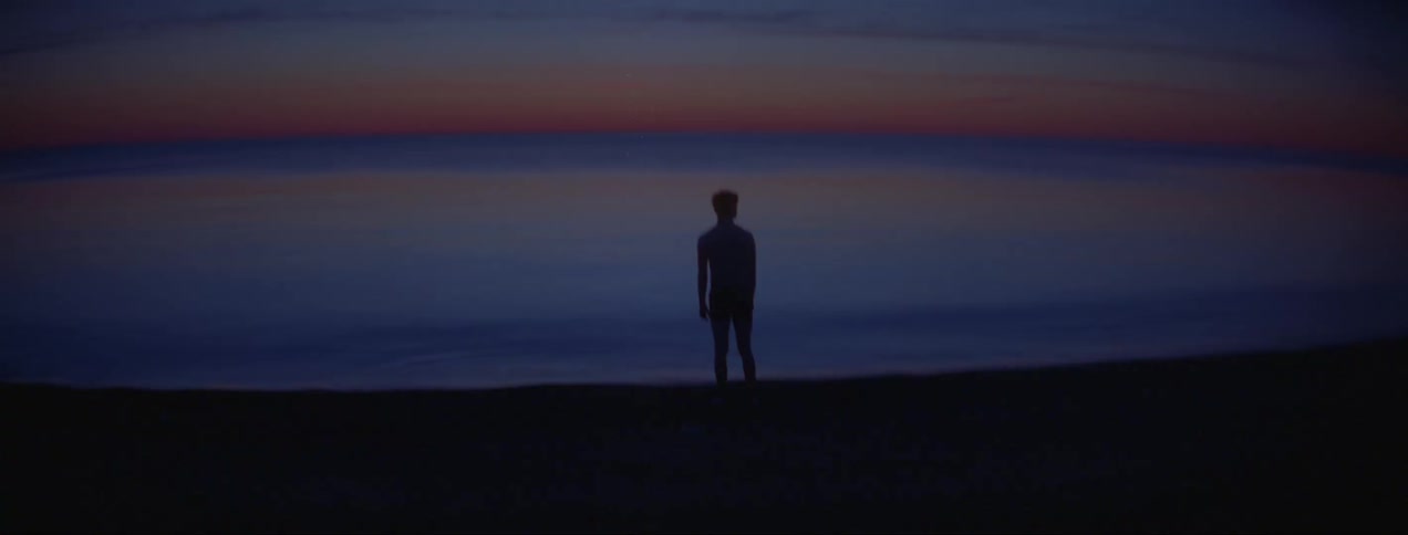 Silhouette of a young man standing on the shoreline at sunset