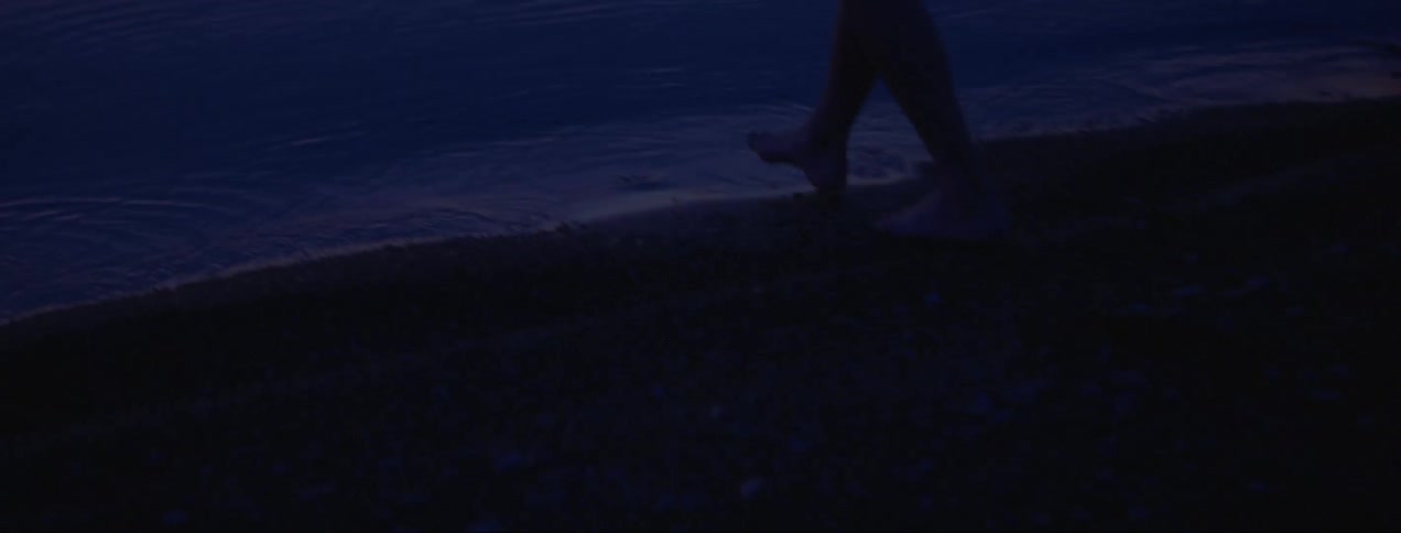 A person gingerly steps into the shallow waters just off of a rocky shoreline