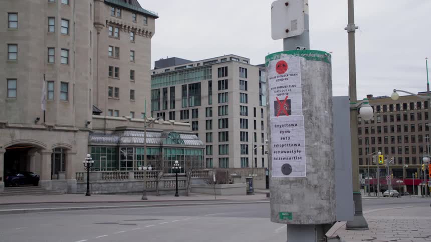 A few cars travel on a city street that is practically empty and a posted sign states that we are stronger than covid 19