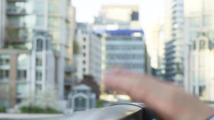 A persons hands drumming on a banister with buildings in the background