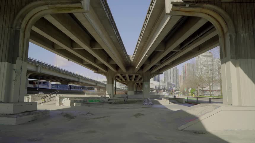 City trains running underneath an overpass with the city skyline in the background