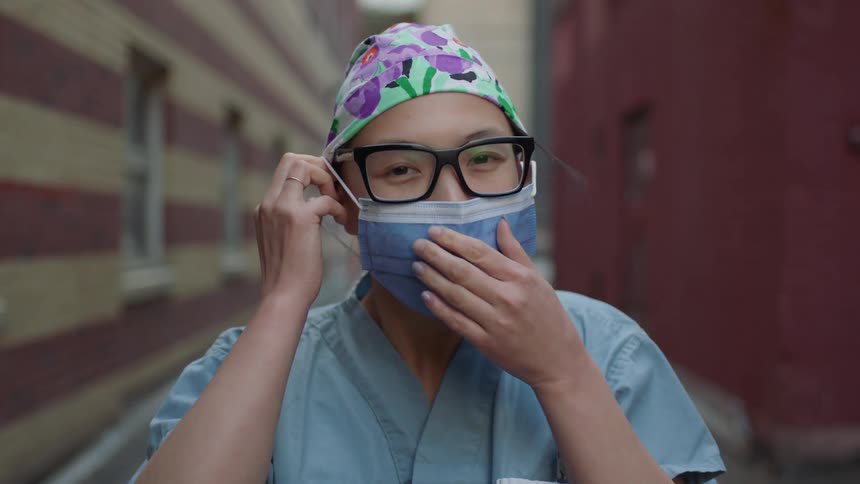 Asian female nurse demonstrates how to wear a face mask in the alley