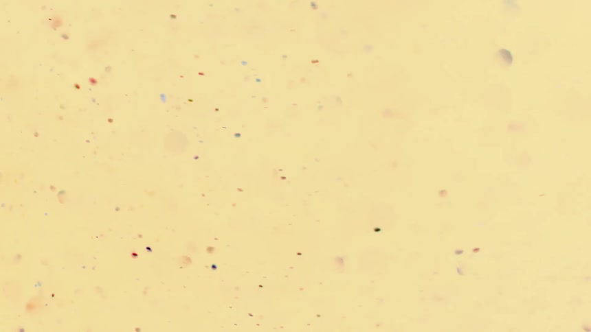 Colorful metallic glitter floats and swirls against light pastel peach background