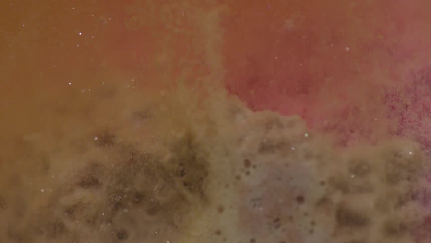 A brown tinted liquid fizzes vigorously as bubble rise upwards through the liquid