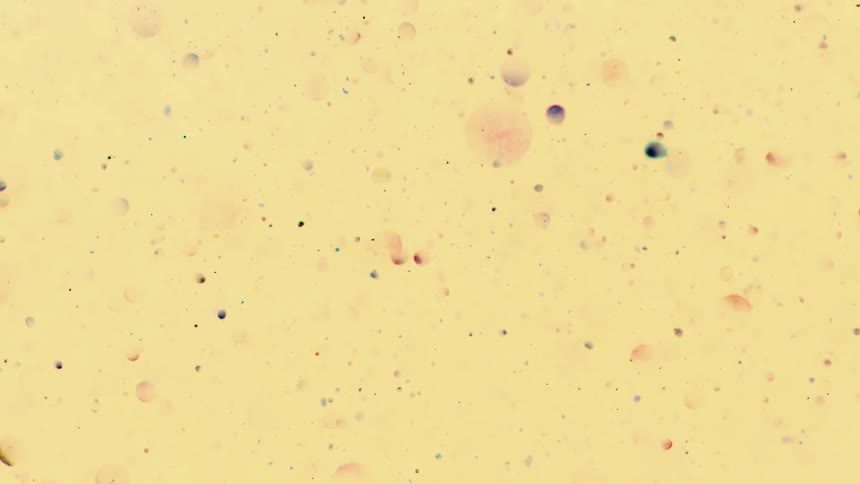 Various colored particles flow through pale yellow orange background