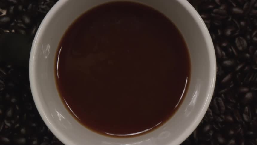 Birds eye view of a cup of coffee on top of coffee beans in a studio