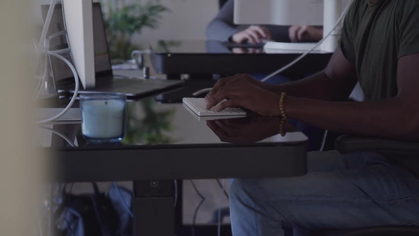 A man sitting on a chair at a desk typing on a keyboard in front of a monitor