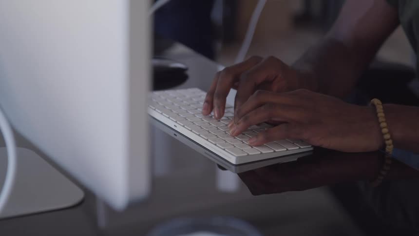 A man sitting at a table typing on a keyboard in front of a monitor