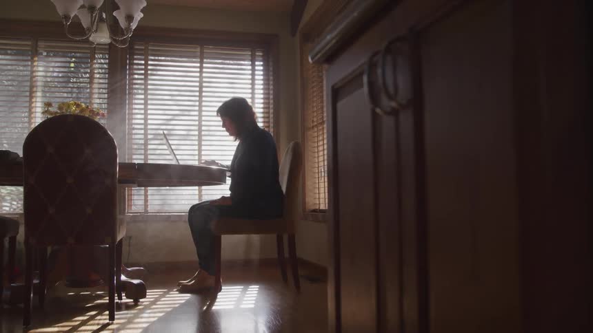 A woman sits at her dining table with a laptop