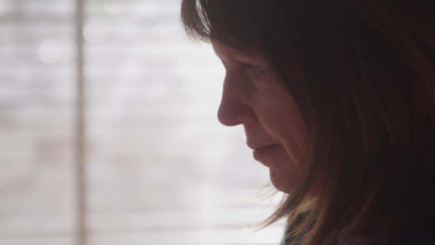 Woman stands near a window pensively in a room at home