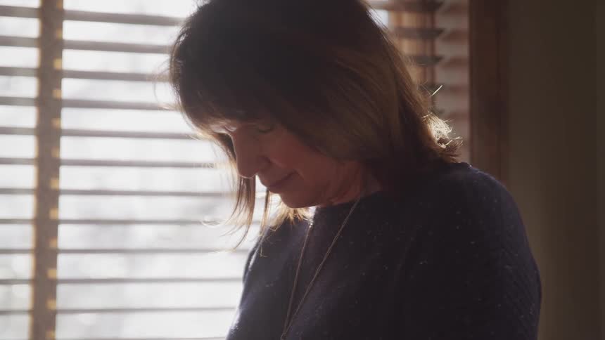 A woman is standing indoors next to a window