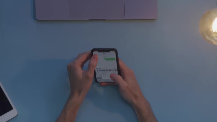A man sits at his desk and types on a smartphone