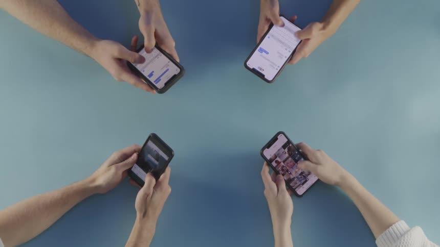 Four people holding smart phones in their hands over a table