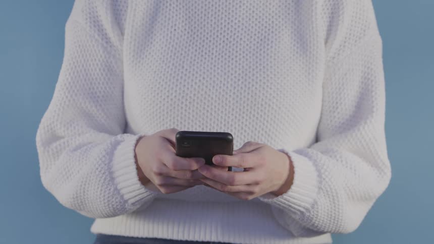 A person wearing a white sweater types on a smartphone to make a call