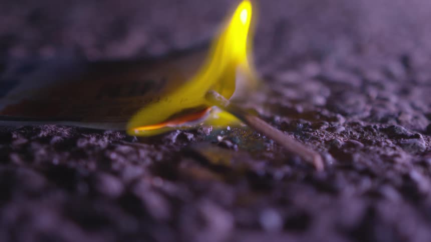 A match and a paper burning with a yellow and blue flame