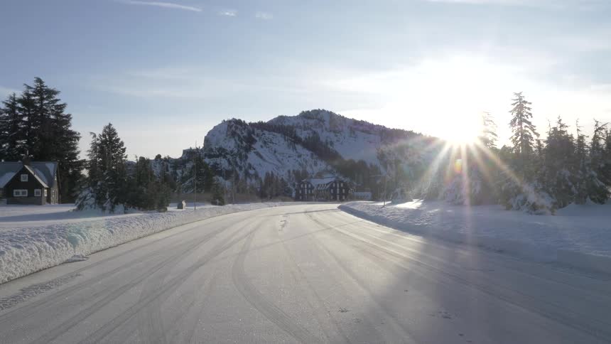 House sits near plowed road decorated by tire tracks and leading toward snow covered mountain