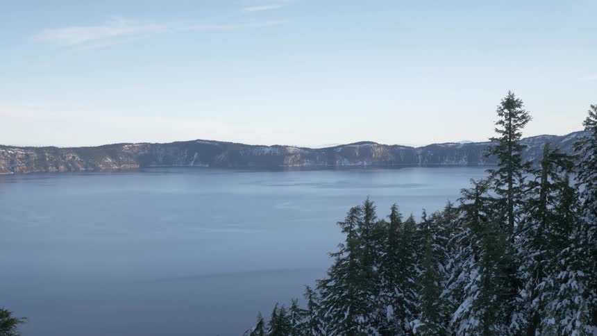 A landscape view of snowy evergreen trees and a lake with hills in the distance