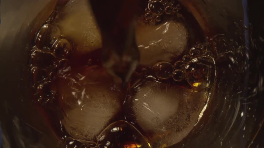 A drink being poured over a glass of ice