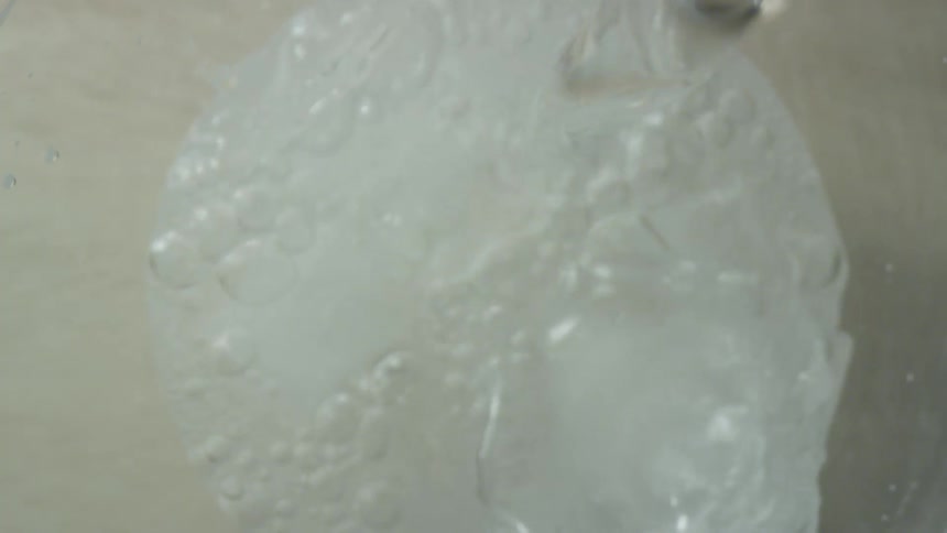 A clear liquid pours into a glass over ice cubes