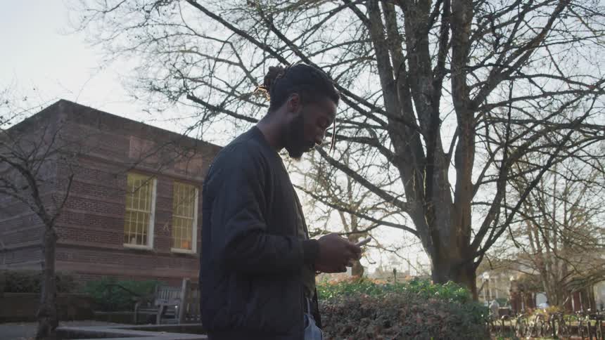 A man stands outside of a home looking at his cell phone
