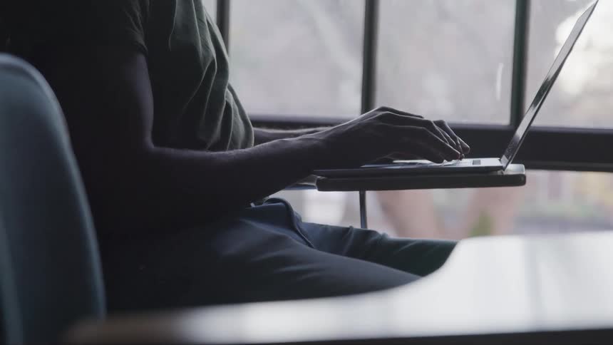 A man sitting in a classroom uses a laptop