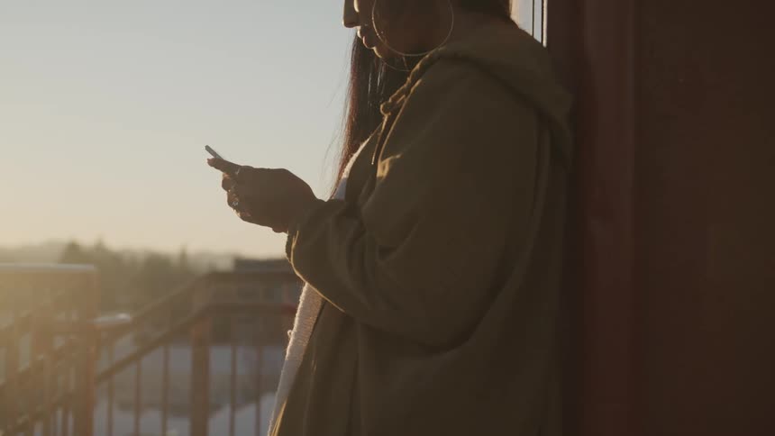 Woman checks her smart phone on the balcony of a building at sunset