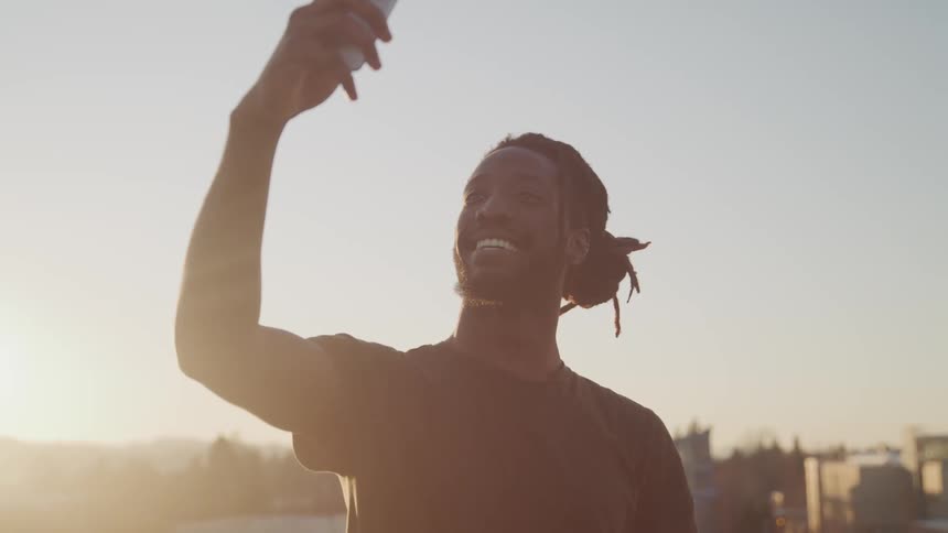 A black man smiles for a selfie while standing outdoors during the day