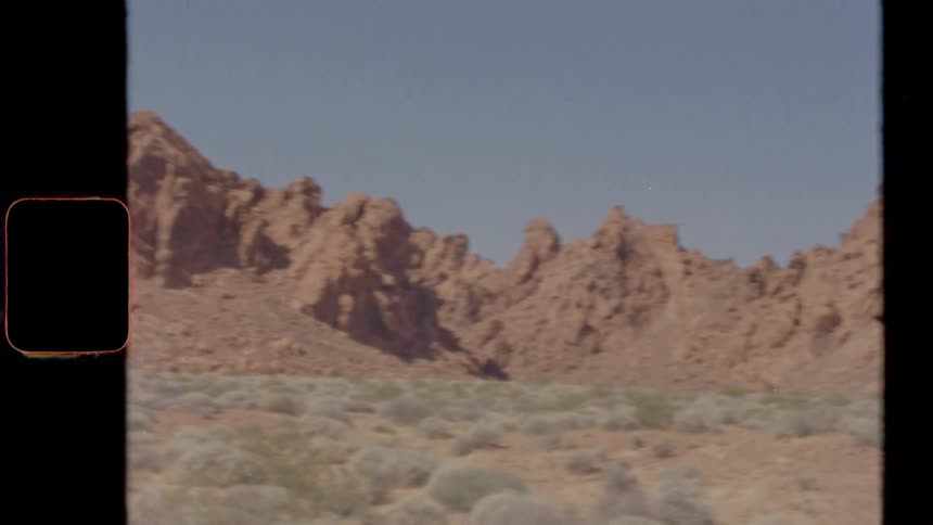 Scrub covers land to rough craggy mountains in badlands under clear sky