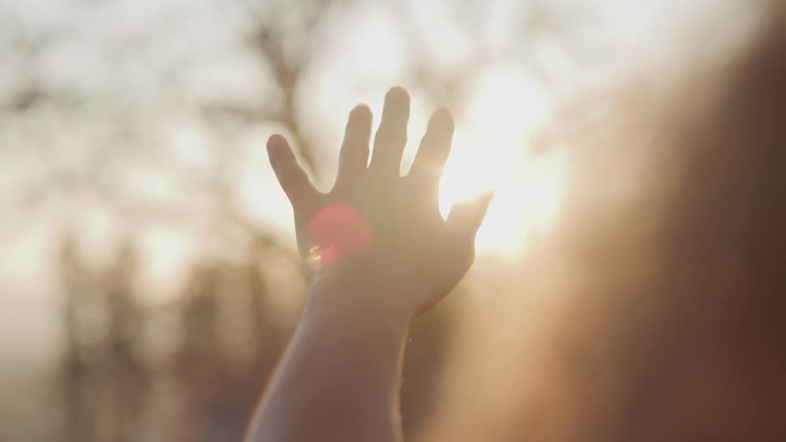 Hand raised in front of sun outdoors