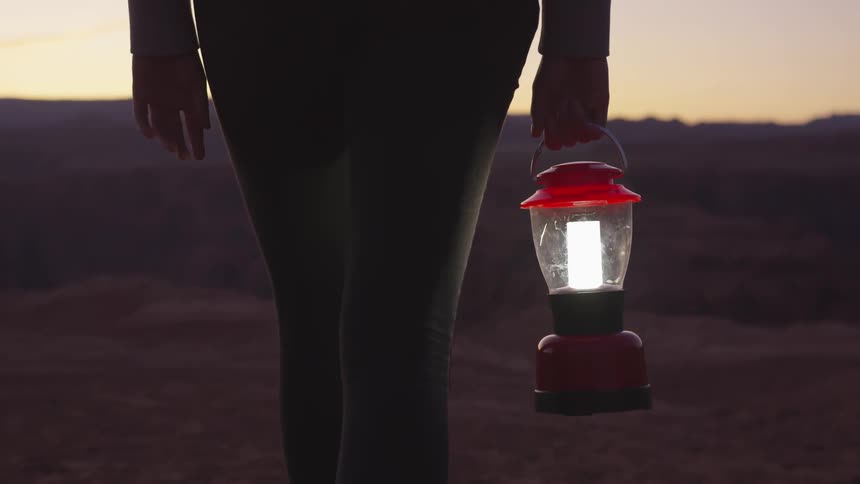A woman walking holding a lantern with a canyon and the sky in the background