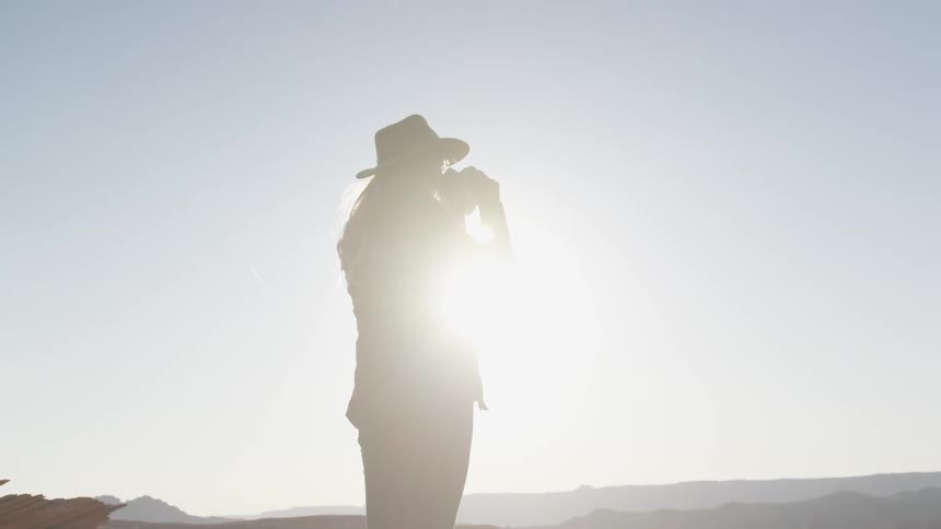 A woman uses binoculars to look out over a canyon on a sunny day