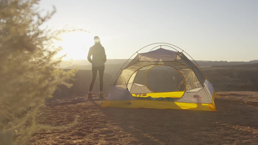 A woman stands outside beside a tent setup in a rural area