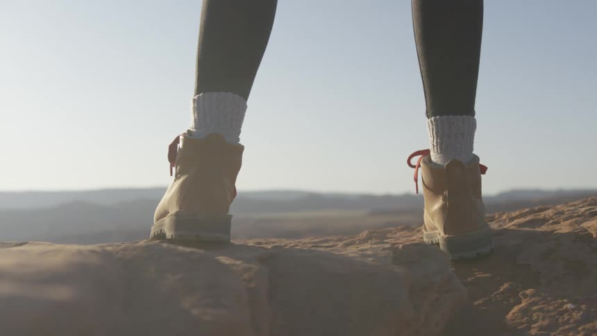 Person stands on stone looking out toward horizon of rough terrain