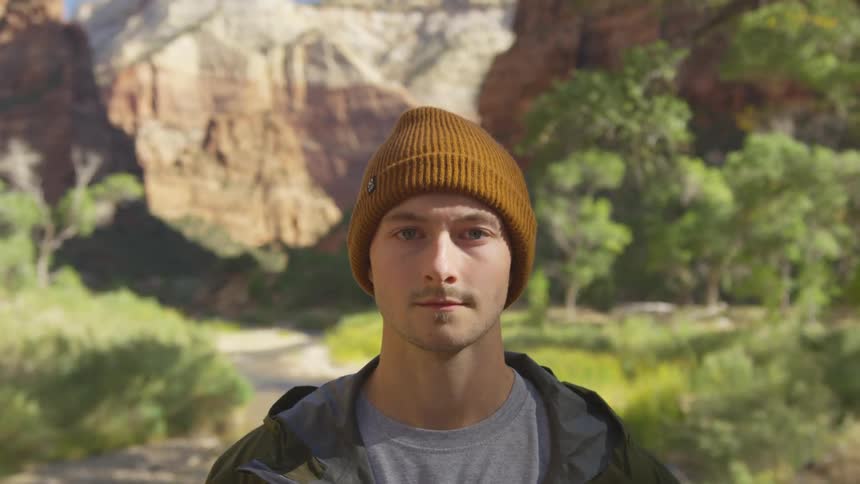 Man stands with back to scenic view of small valley surrounded by steep cliffs